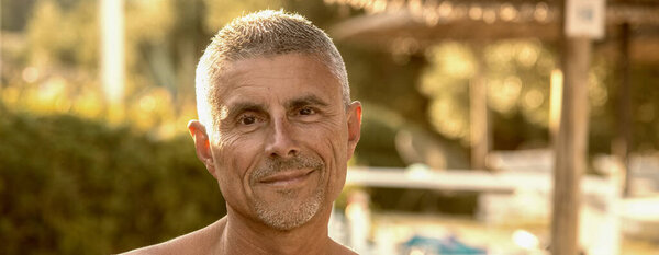 Smiling man relaxing on the beach in summer season. Straw beach umbrella in the background.