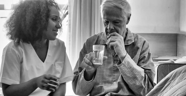 病院のベッドで老人に薬を与えるアフリカの女性医師 リハビリテーションと退職の概念 — ストック写真