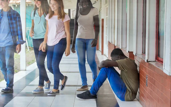 Young boy sitting alone with sad feeling at school. African child in depression abandoned in a corridor and leaning against brick wall. Bullying, discrimination and racism concept.