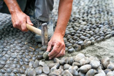 Yol çalışıyor. Adam çekiçle eski yola çakıl taşları koyar..