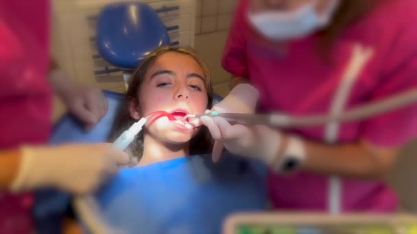歯医者の手を閉じる患者のブラケットに弾性ゴムバンドを置く 歯に配線された金属のブレースを持つ女の子が矯正治療を受けて — ストック動画
