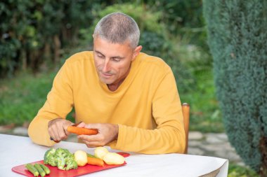 Kafkasyalı adam akşam yemeği için salata malzemeleri hazırlamak için havuç dilimliyor..
