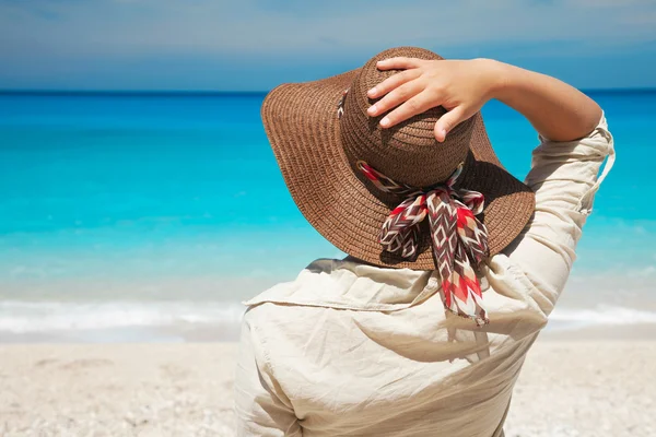 Mujer joven de pie en la playa sosteniendo su sombrero y mirando a un mar — Foto de Stock