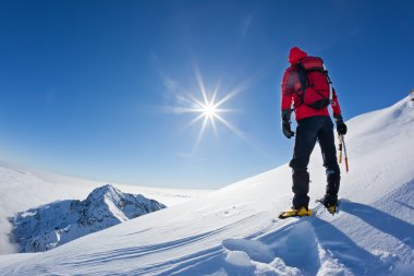 Mountaineer reaches the top of a snowy mountain in a sunny winte clipart