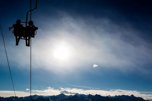 Twee skiërs in een stoeltjeslift verlicht door de zon. — Stockfoto
