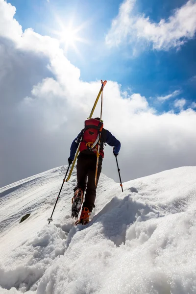 Ski bergsbestigare gå upp längs en brant snöig bergskam med s Stockbild