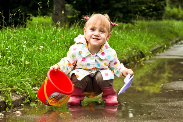 Cute little girl is playing in muddy puddles — Stock Photo, Image