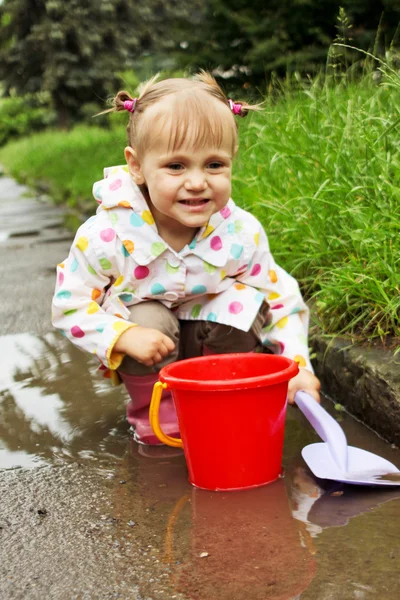 泥だらけの水たまりでかわいい女の子を再生します。 — ストック写真