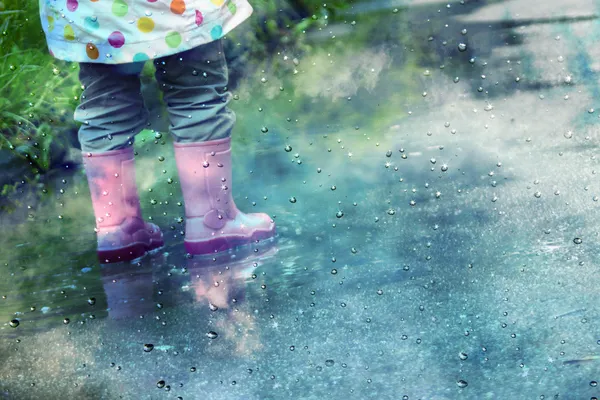 Söt liten flicka spelar i leriga pölar — Stockfoto