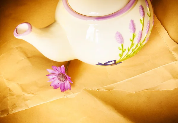 Teekanne und violette Blume auf altem Papier Hintergrund — Stockfoto