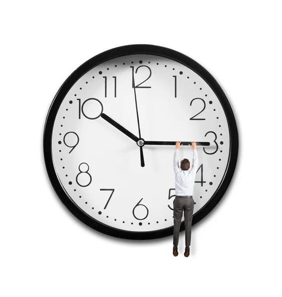 Businessman hanging from the hands of a clock — Stock Photo, Image