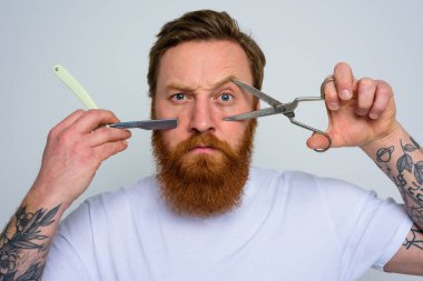 Makas ve bıçaklı endişeli adam sakalı kesmeye hazır.