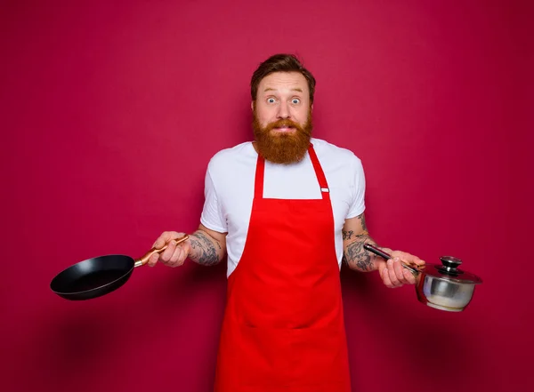 Chef effrayé avec barbe et tablier rouge cuisiniers avec poêle et pot — Photo