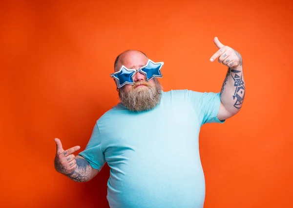 Fat delusion man with beard, tattoos and sunglasses is uncertain for something — Stock Photo, Image