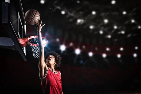 Jogador de basquete em uniforme vermelho pulando alto para fazer um slam dunk para a cesta — Fotografia de Stock