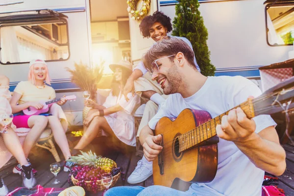 Vrienden picknicken met een camper en spelen met gitaar — Stockfoto