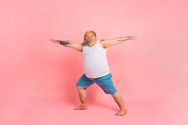 Lustiger Mann mit Bart in Yoga-Stellung auf rosa Studiohintergrund — Stockfoto