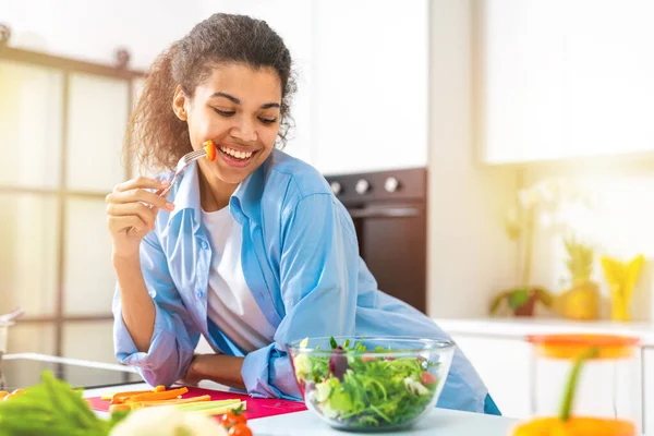 Mutfakta taze sebzeli salata yiyen genç bir kadın. — Stok fotoğraf