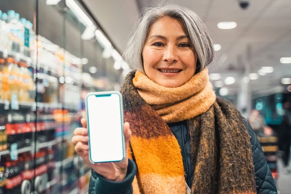 Senior woman at the supermarket shows the screen of her smartphone — Stock fotografie