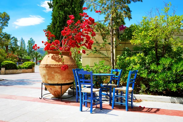 Die Amphore mit Blumen und traditionellen griechischen Tisch und Stühlen — Stockfoto