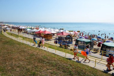 KORNOMORSK, UKRAINE - 8 Ağustos 2021 'de Ukrayna' nın Chornomorsk kentinde insanlar bir plajda güneşlenmeye ve Karadeniz 'de yüzmeye gidiyorlar.. 