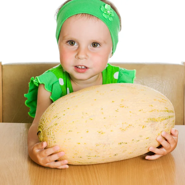 Little girl sitting at a table with a big melon — Stock Photo, Image