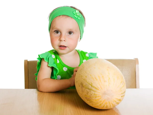 Little girl sitting at a table with a big melon — Stock Photo, Image