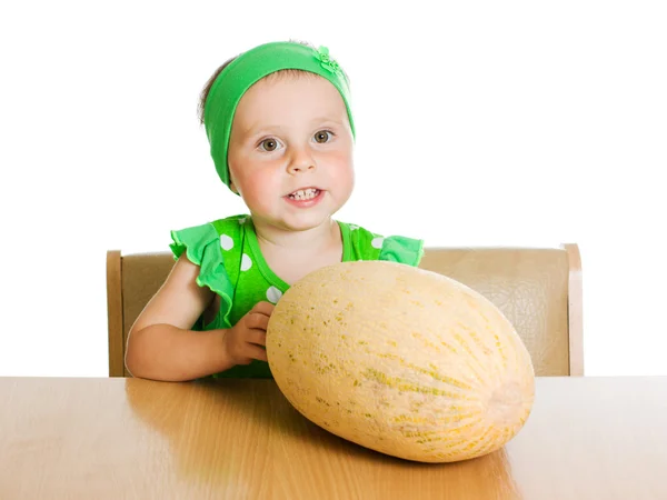 Little girl sitting at a table with a big melon — Stock Photo, Image