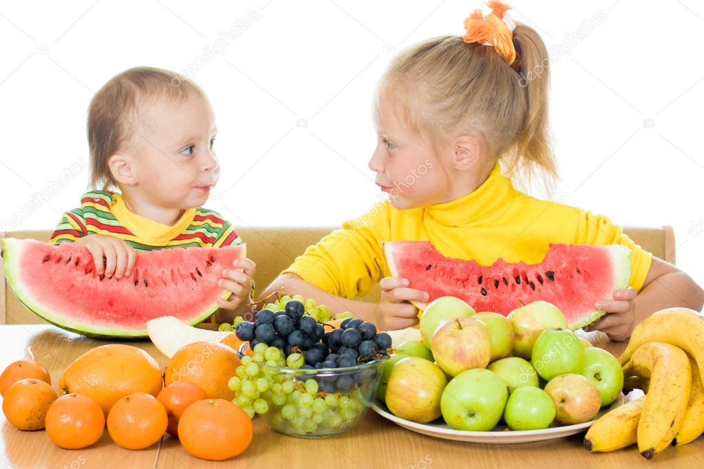 Two children eat fruit at a table