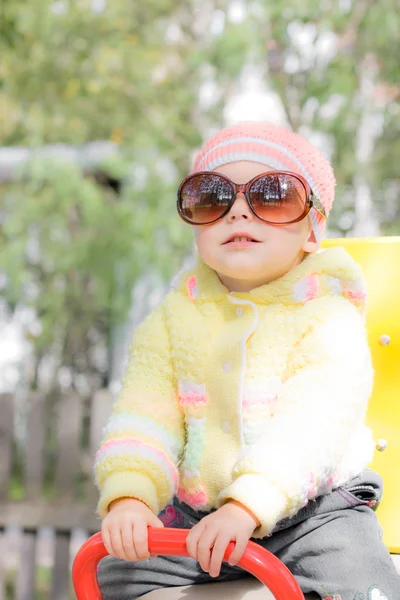 Kid wearing sunglasses on swing — Stock Photo, Image