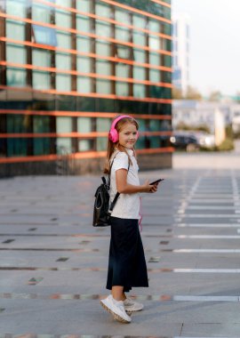 a girl in pink headphones and with a backpack walks around the city
