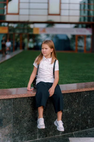a girl in a shirt and shorts is sitting in the park with a backpack