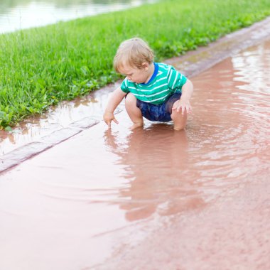 Child sits in a puddle and by means of a finger defines depth clipart