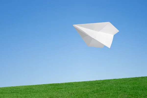 Avión de papel volando sobre el césped contra el cielo azul — Foto de Stock