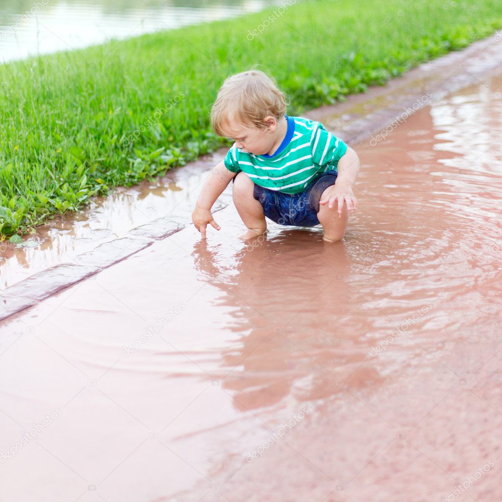 Child sits in a puddle and by means of a finger defines depth