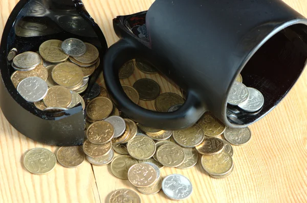 Broken mug and coins on a table — Stock Photo, Image