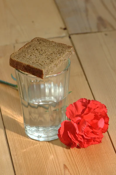 Copo de vodka e cravos vermelhos em uma mesa de madeira — Fotografia de Stock