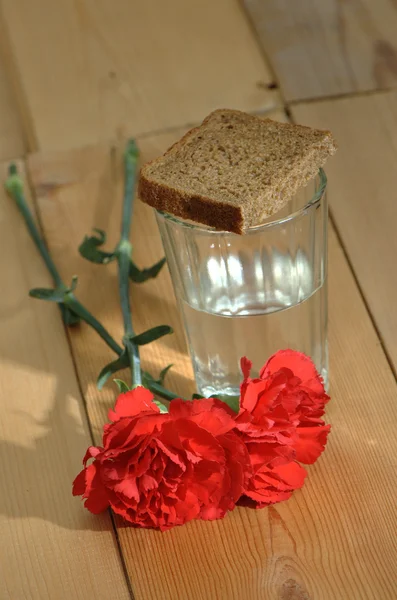 Ποτήρι βότκα και κόκκινα γαρίφαλα σε ένα ξύλινο τραπέζι — Φωτογραφία Αρχείου