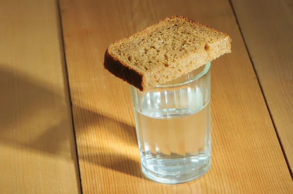 Glas wodka en een sneetje brood op een houten tafel — Stockfoto