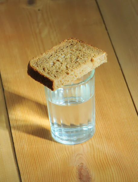 Glas Wodka und eine Scheibe Brot auf einem Holztisch — Stockfoto