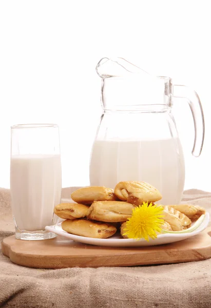 Glaskrug mit frischer Milch und gelben Blumen auf weißem Hintergrund — Stockfoto