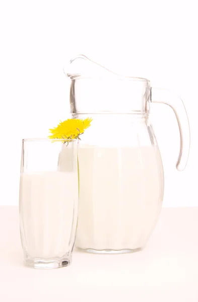 Glas kruik met verse melk en gele bloemen op witte achtergrond — Stockfoto