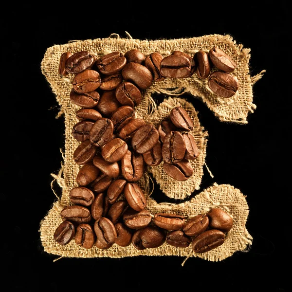 Alphabet from coffee beans on fabric texture isolated on black — Stock Photo, Image