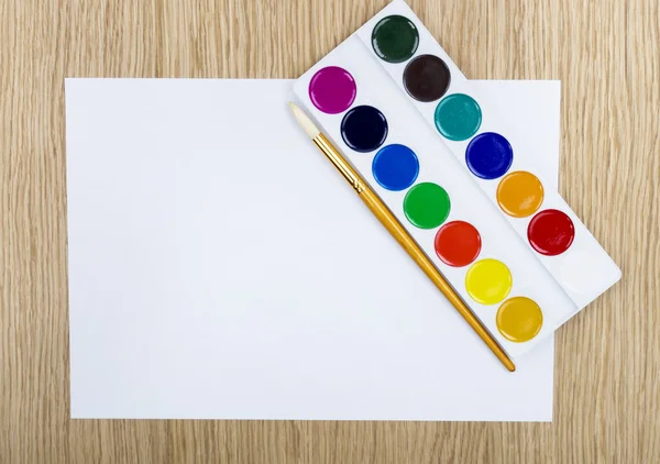 Farby i pędzel na białym papierze — Zdjęcie stockowe