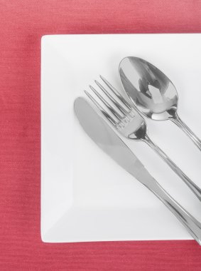 beyaz boş tabak çatal, kaşık ve bıçak üzerinde kırmızı bir masa örtüsü