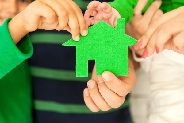 Family of four holding green house in hands — Stock Photo, Image