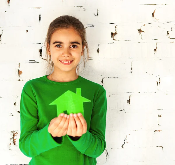 Маленькая улыбающаяся брюнетка держит в руках зеленый дом — стоковое фото