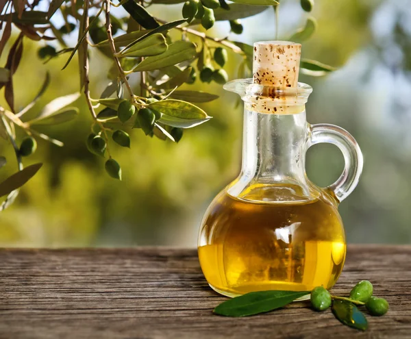 Aceite de oliva y rama de olivo sobre la mesa de madera — Foto de Stock