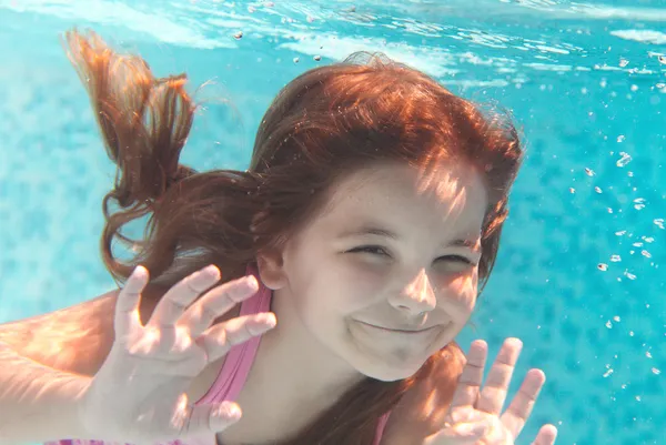Das kleine Mädchen schwimmt unter Wasser und lächelt — Stockfoto