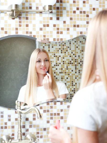 Mujer joven aplicando lápiz labial mirando al espejo — Foto de Stock